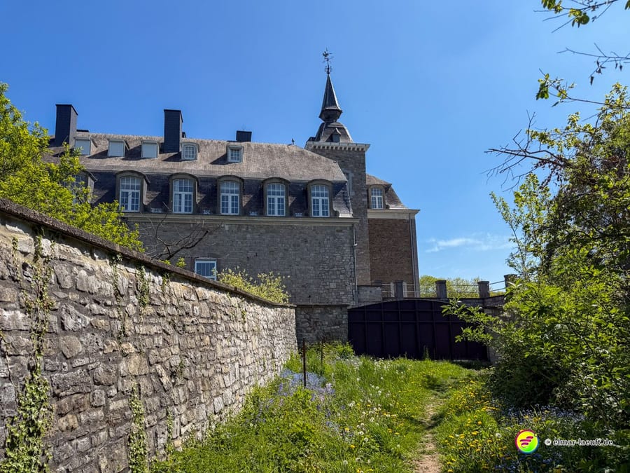 Große Klosteranlage mit Schieferdach und Dachreiter hinter einer hohen Bruchsteinmauer.