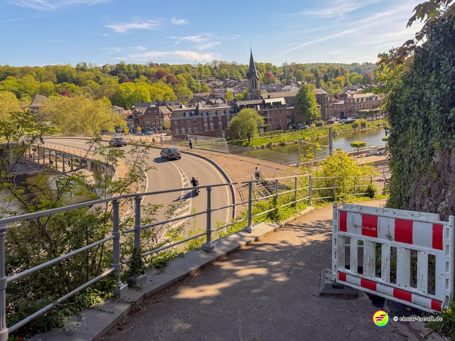 Von oben auf den Ort mit Kirchturm, Straße und einer rot-weißen Absperrung.
