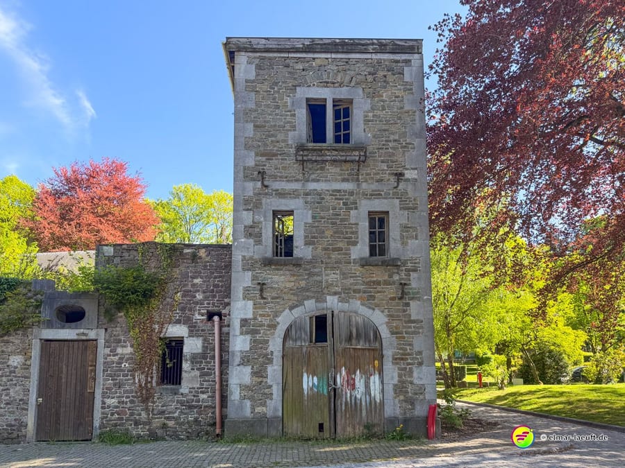 Turmartiges Bruchsteinhaus mit hölzernem Tor und roten Blutbuchen daneben.