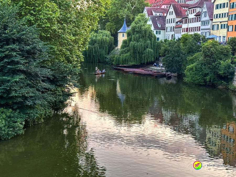 Laufen entlang des ruhigen Flusses in Tübingen mit Blick auf grüne Bäume und bunte Fachwerkhäuser am Ufer.