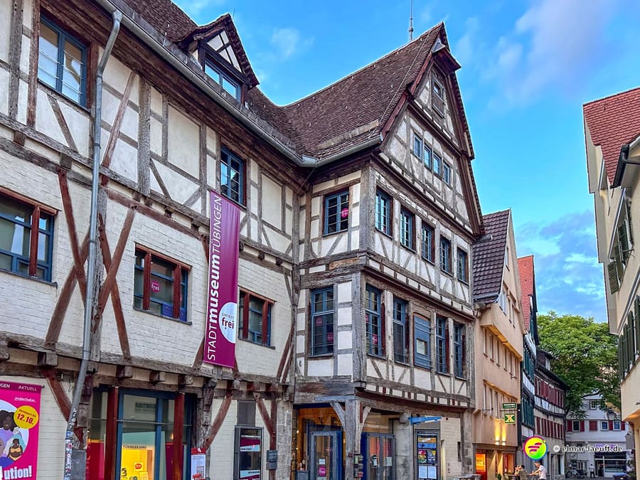 Laufen durch die historische Altstadt von Tübingen mit Fachwerkhäusern und einem blauen Himmel im Hintergrund.