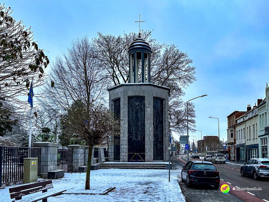 Laufen in Heerlen an einem winterlichen Tag mit leicht verschneitem Boden und einer markanten Kapelle neben einer ruhigen Straße mit Häusern und parkenden Autos.
