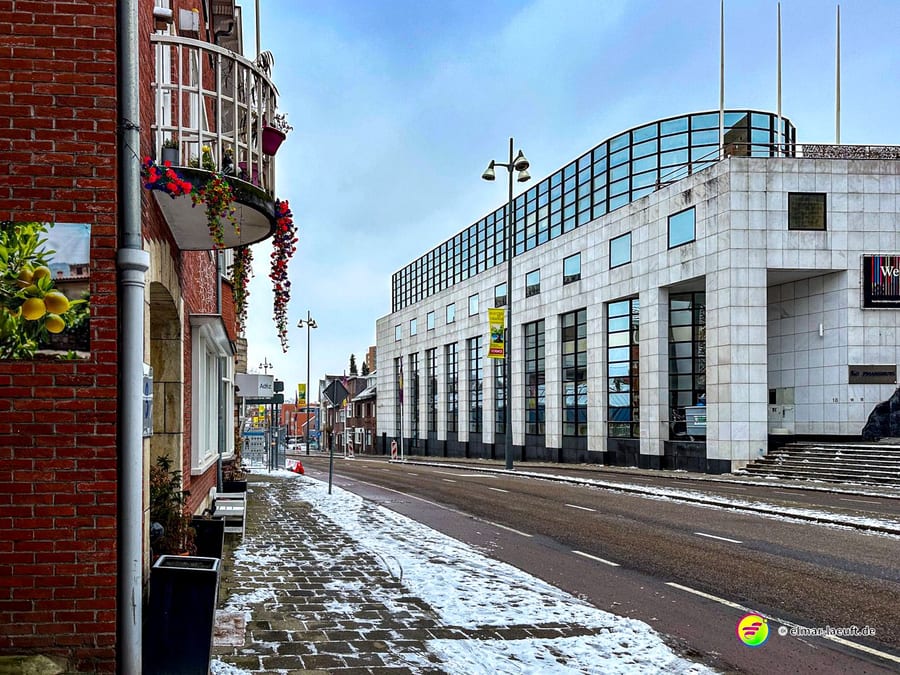 Laufen auf einem schneebedeckten Bürgersteig entlang einer ruhigen Straße mit modernen und traditionellen Gebäuden in Heerlen.