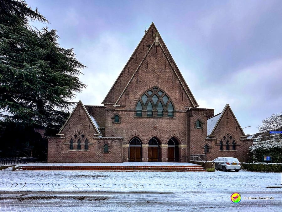Laufen in Heerlen vor einer großen, dreieckigen Backstein-Kirche bei winterlicher Schneedecke auf dem Boden.