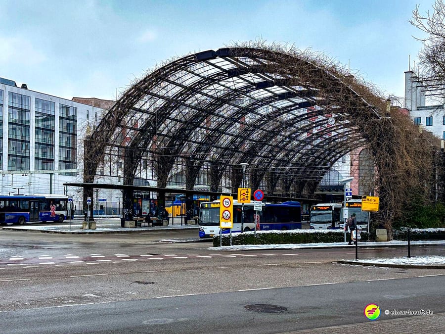 Laufen in Heerlen führt an einer ungewöhnlichen, mit Pflanzen bewachsenen Stahlkonstruktion vorbei, die als Überdachung für mehrere Busse in einer urbanen Umgebung dient.