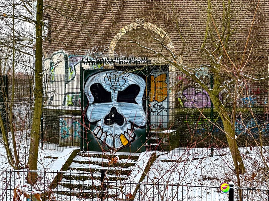 Laufen in Heerlen führt an einem mit Schnee bedeckten, verlassenen Gebäude vorbei, dessen Eingang von einem großen, bunten Totenkopf-Graffiti geprägt ist.