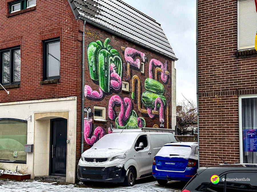 Laufen durch eine verschneite Stadtstraße in Heerlen mit bunter Graffiti-Kunst an einer Hauswand und geparkten Autos.
