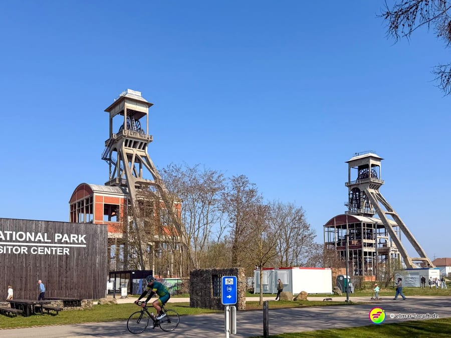 Läufer passiert eine ehemalige Industrieanlage mit hohen Förderturmstrukturen bei Maasmechelen an einem klaren Tag.