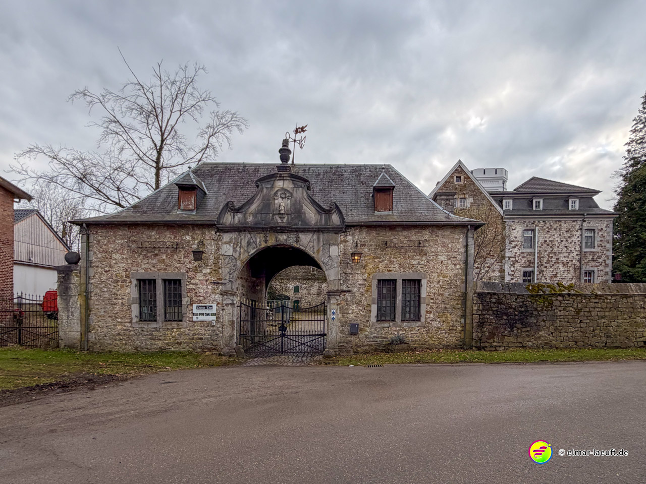 Historisches Steintor mit barockem Giebel und Wappen als Eingang zu einem Anwesen. Das verwitterte Torhaus aus Bruchstein markiert den repräsentativen Zugang zu einem Herrensitz.