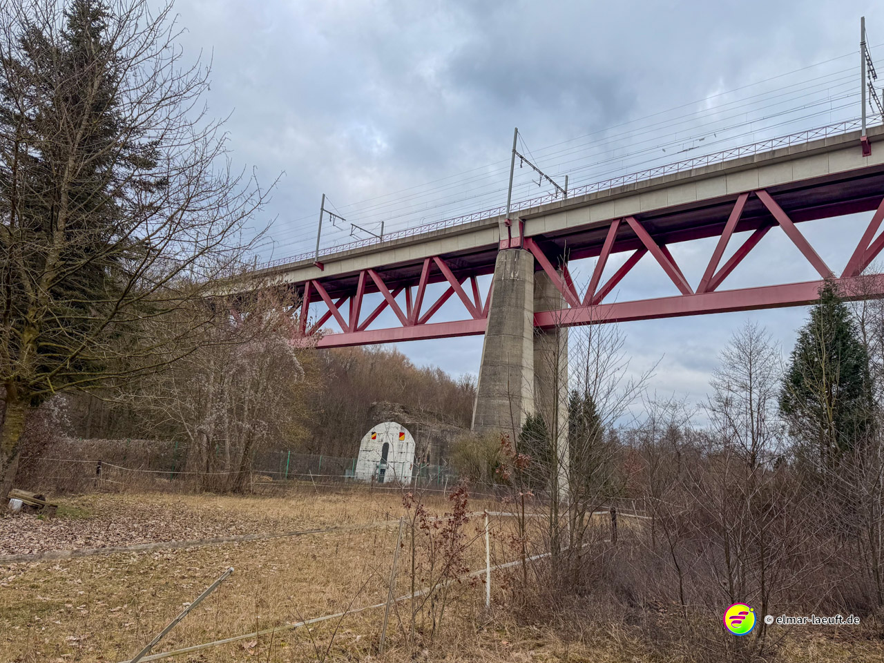 Moderne Eisenbahnbrücke mit roter Stahlkonstruktion über bewaldetes Tal. Die Hochbrücke mit charakteristischen Fachwerkträgern ist Teil der wichtigen Bahnstrecke im deutsch-belgischen Grenzgebiet.
