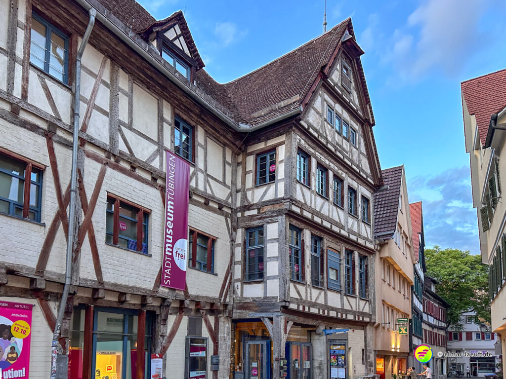 Laufen durch die historische Altstadt von Tübingen mit Fachwerkhäusern und einem blauen Himmel im Hintergrund.