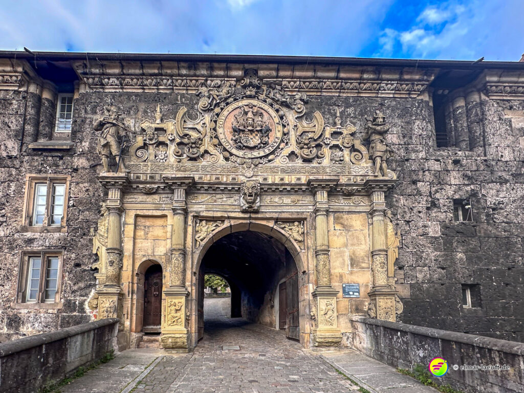Laufen durch das kunstvoll verzierte Stadttor in Tübingen auf Kopfsteinpflaster unter blauem Himmel.