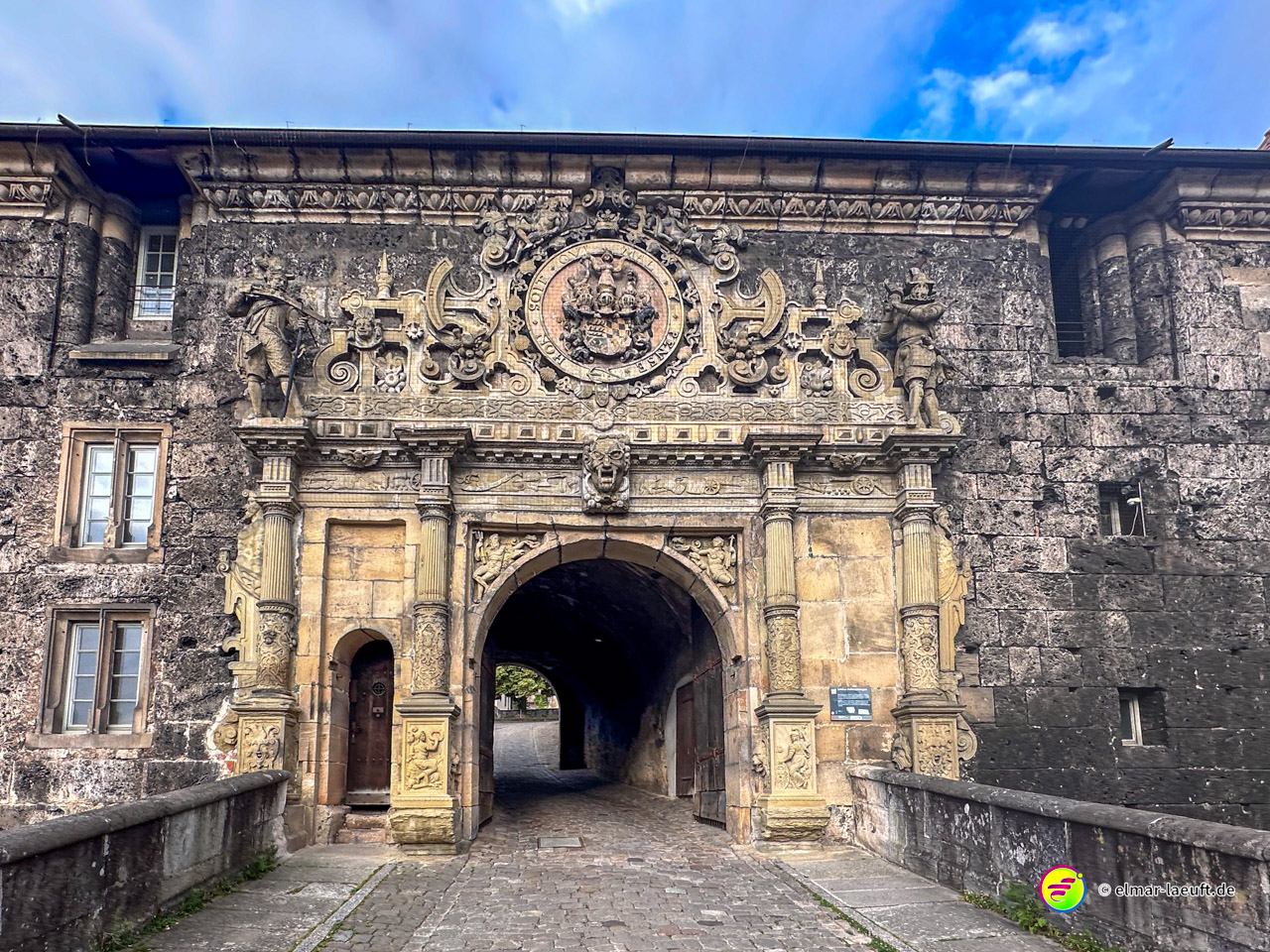 Laufen durch das kunstvoll verzierte Stadttor in Tübingen auf Kopfsteinpflaster unter blauem Himmel.