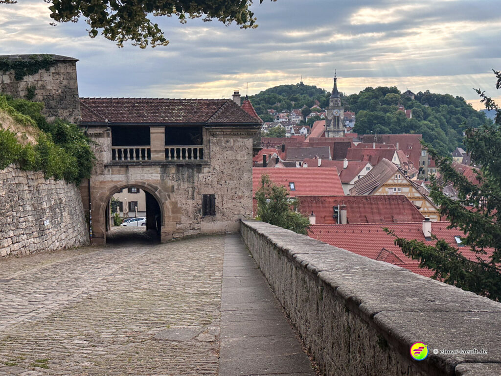 Laufen auf einem gepflasterten Weg mit historischem Torbogen und Blick auf die Altstadt von Tübingen bei bewölktem Himmel.