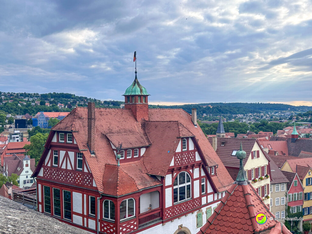 Laufen in Tübingen mit Blick auf historische Fachwerkhäuser und die grüne Hügellandschaft im Hintergrund unter einem bewölkten Himmel.
