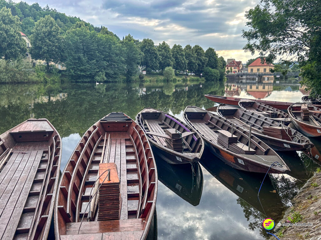 Laufen am ruhigen Neckar in Tübingen mit Blick auf mehrere festgemachte Holzboote und eine grüne Uferlandschaft bei bewölktem Himmel.
