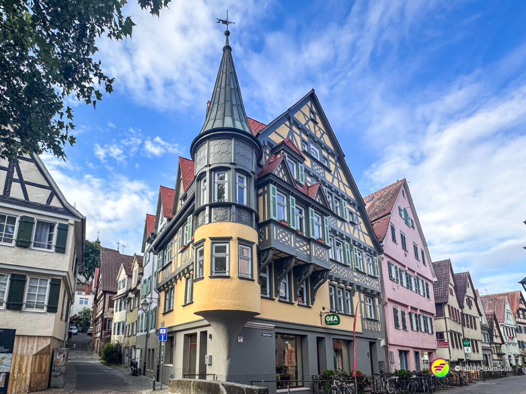Laufen durch die historische Altstadt von Tübingen mit Fachwerkhäusern und einem markanten Turm bei blauem Himmel.
