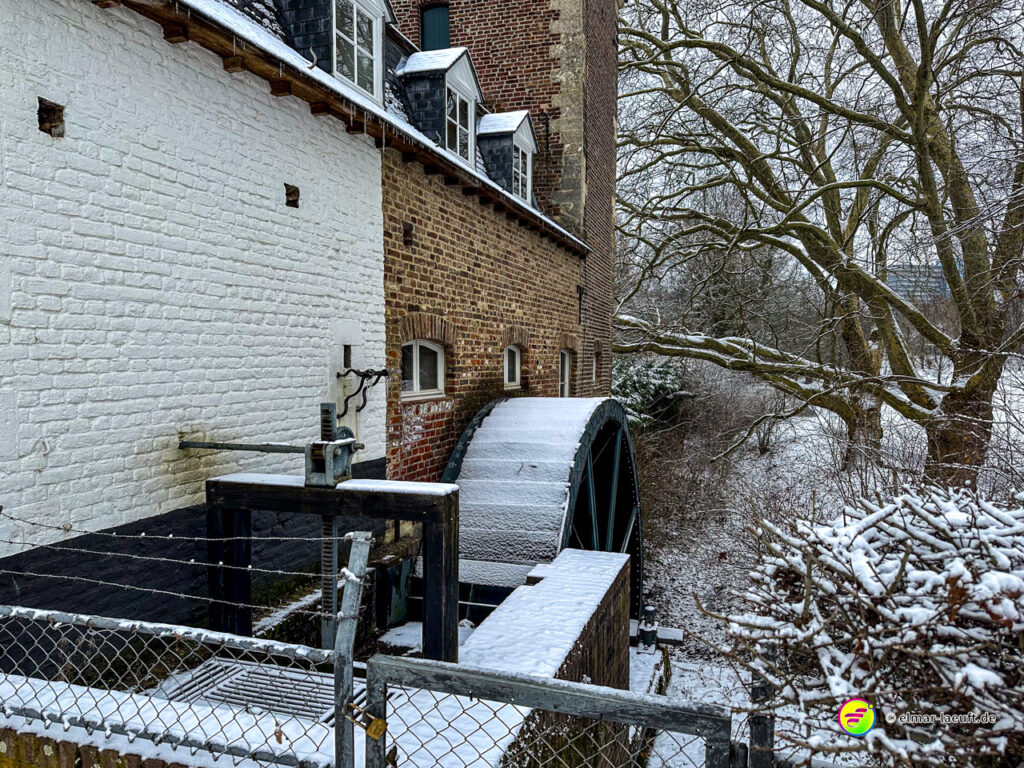 Laufen im winterlichen Heerlen vorbei an einer alten Mühle mit schneebedecktem Wasserrad und verschneiter Natur im Hintergrund.