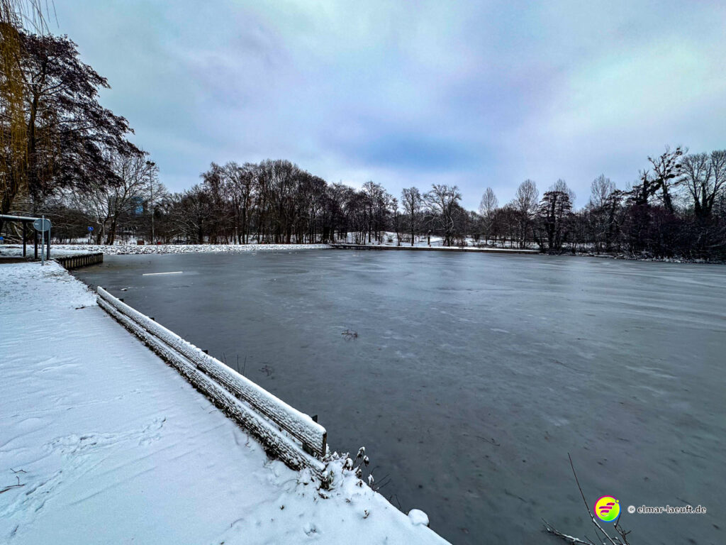 Laufen an einem zugefrorenen See in einer verschneiten Parklandschaft mit kahlen Bäumen in Heerlen.