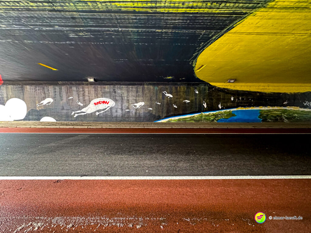 Laufen auf einem asphaltierten Weg unter einer Brücke mit bunter Wandmalerei in einer urbanen Umgebung in Heerlen.
