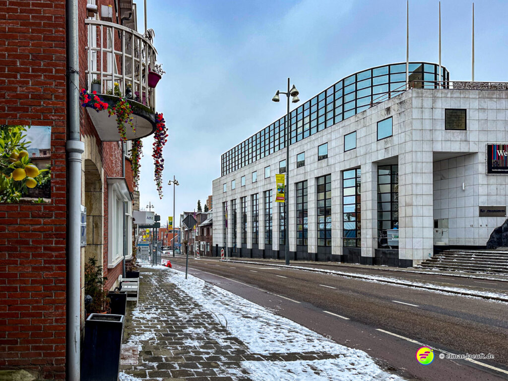 Laufen auf einem schneebedeckten Bürgersteig entlang einer ruhigen Straße mit modernen und traditionellen Gebäuden in Heerlen.