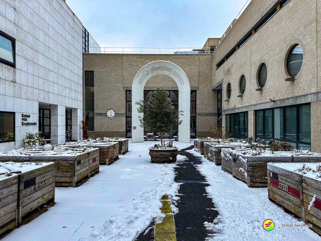 Laufen auf einem schmalen, schneebedeckten Pfad zwischen modernen Gebäuden und bepflanzten Holzkästen in Heerlen.