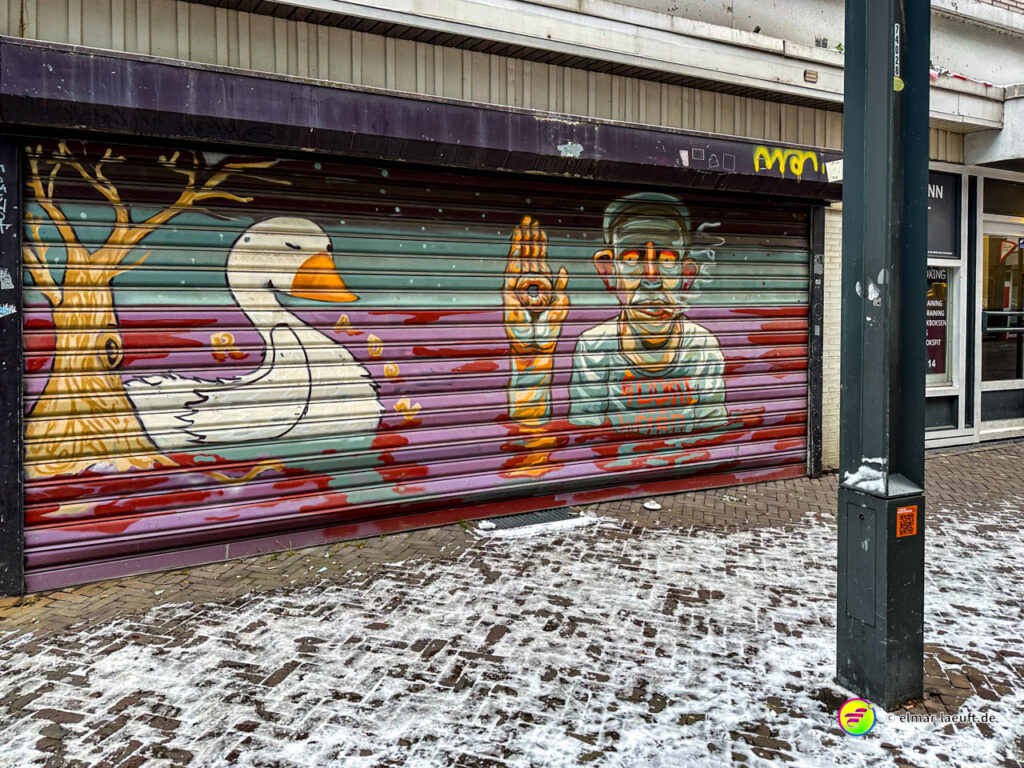 Laufen in Heerlen an einem winterlichen Tag mit leicht verschneitem Kopfsteinpflaster und bunter Graffiti-Kunst auf einem geschlossenen Ladenrolltor.
