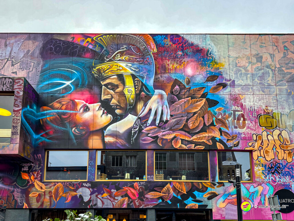 Laufen in Heerlen vorbei an einer bunten Hauswand mit großem Wandgemälde eines römischen Soldaten und einer Frau in urbaner Umgebung.