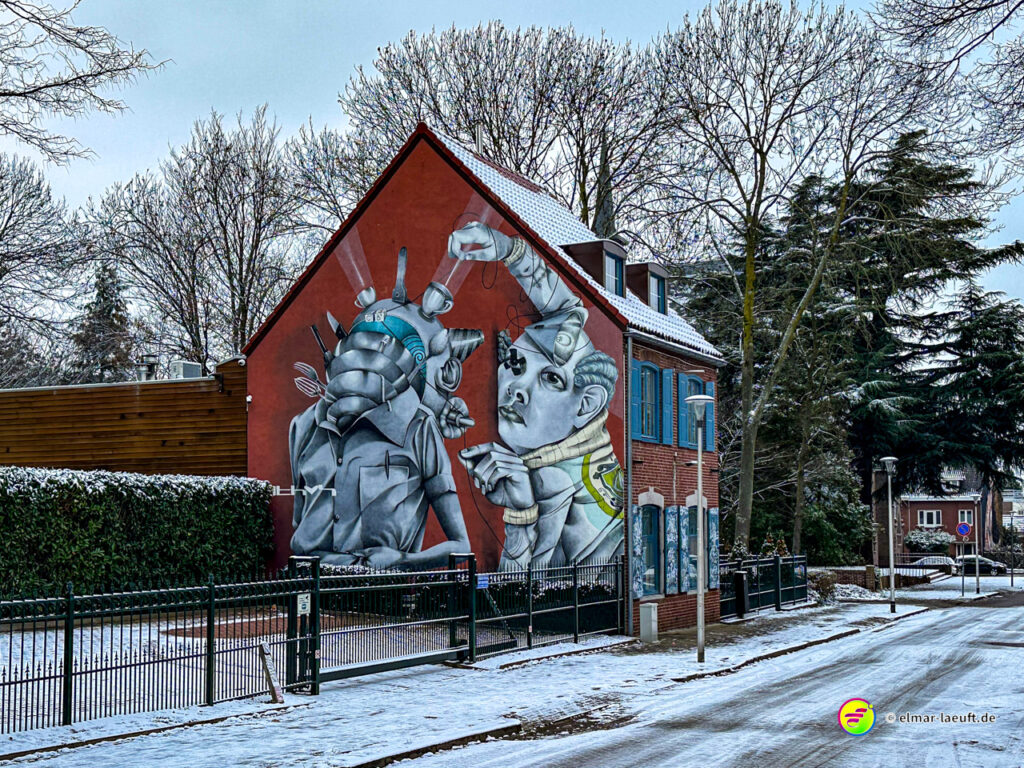 Laufen in Heerlen an einem winterlichen Straßenrand mit einem Haus, das eine große, künstlerische Wandmalerei zeigt.