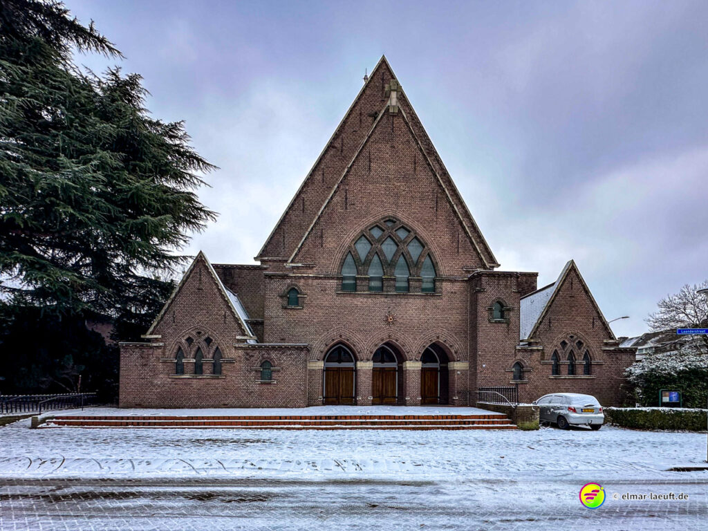 Laufen in Heerlen vor einer großen, dreieckigen Backstein-Kirche bei winterlicher Schneedecke auf dem Boden.
