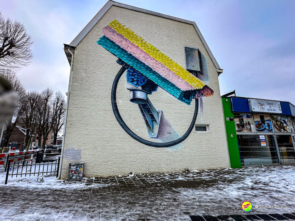 Laufen in Heerlen bei winterlicher, schneebedeckter Straße mit bunter Wandmalerei an einem Haus in urbaner Umgebung.