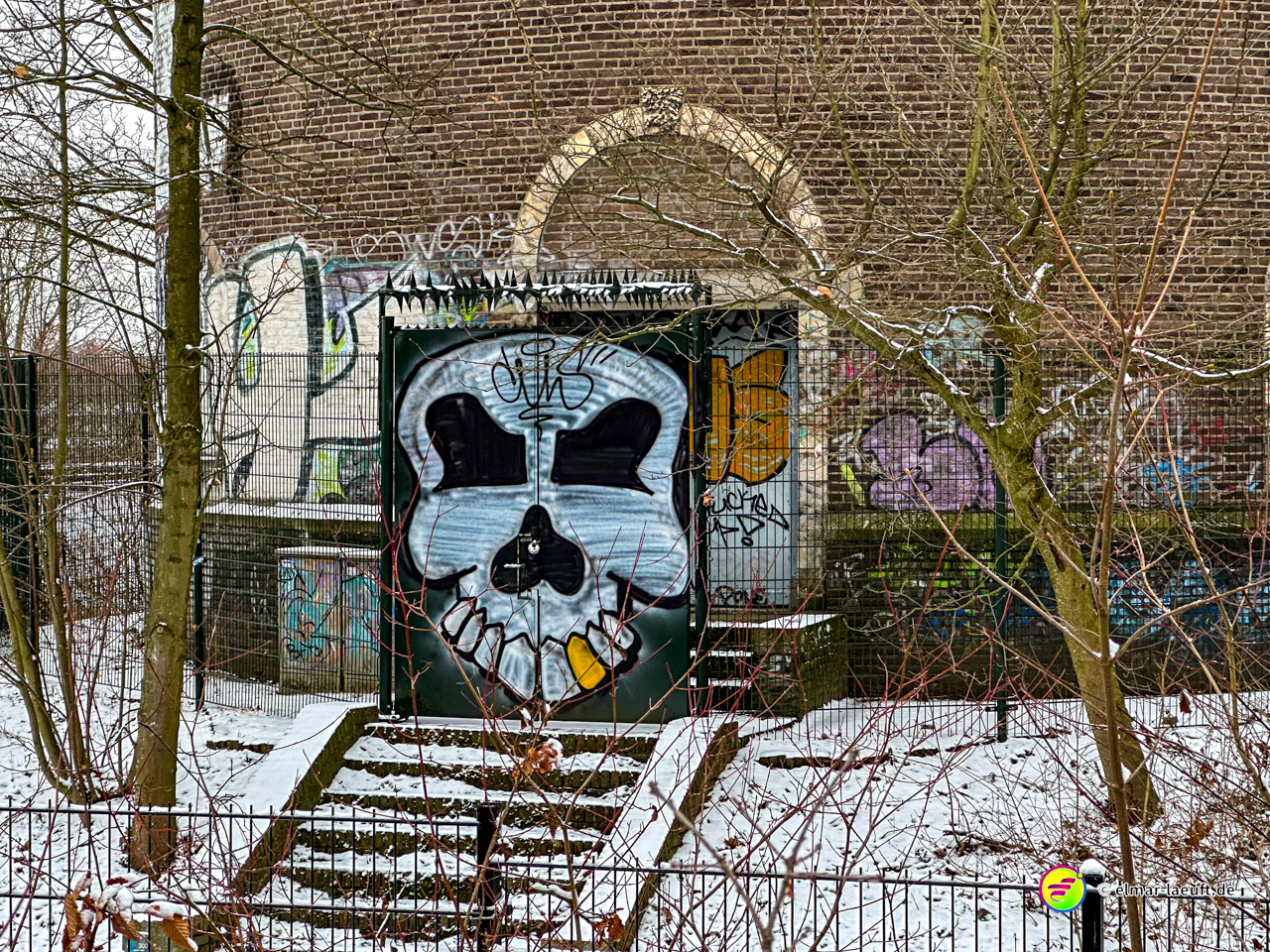 Laufen in Heerlen führt an einem mit Schnee bedeckten, verlassenen Gebäude vorbei, dessen Eingang von einem großen, bunten Totenkopf-Graffiti geprägt ist.