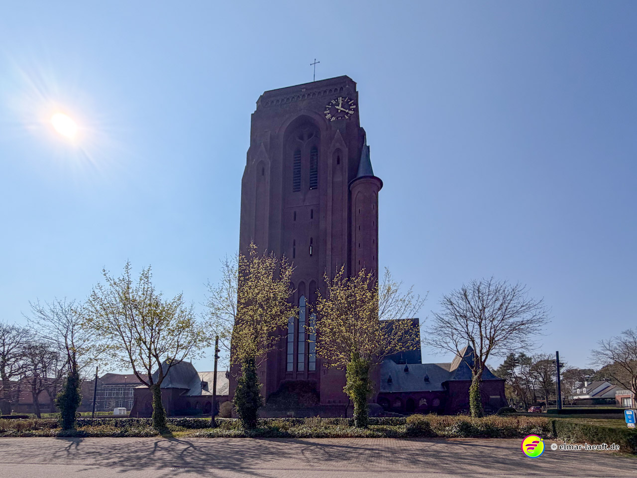 Beim Laufen in Maasmechelen zeigt sich ein großer, historischer Kirchturm bei strahlendem Sonnenschein und klarem Himmel.