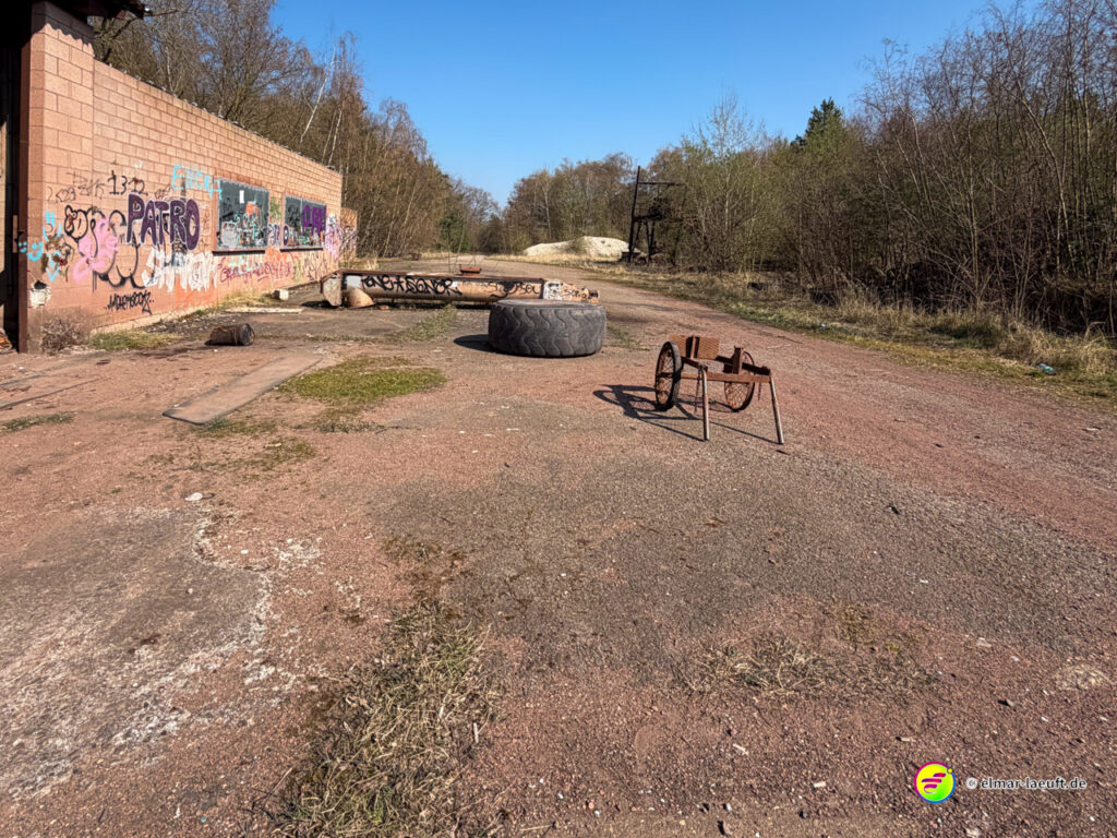 Laufen auf einem verlassenen, mit Graffiti bedeckten Industrieareal in Maasmechelen mit alten Reifen und Metallgestellen auf dem Weg unter blauem Himmel.