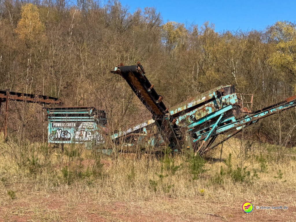 Beim Laufen in Maasmechelen führt der Weg an einer verlassenen, rostigen Förderanlage vorbei, umgeben von trockenem Gras und kahlen Bäumen.
