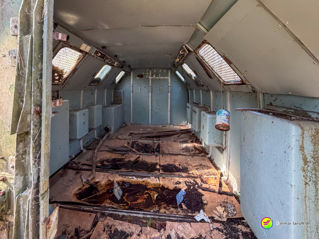 Beim Laufen in Maasmechelen entdecke ich den verlassenen Innenraum eines alten, rostigen Fahrzeugs mit verrosteten Metallwänden und zerfallenem Boden.