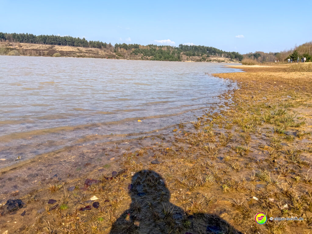 Laufen am Ufer eines ruhigen Sees mit weiter Sicht auf bewaldete Hügel bei Maasmechelen.